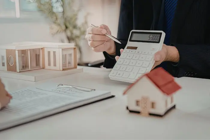 Personne tenant calculatrice et stylo devant contrat, image liée à l'achat immobilier