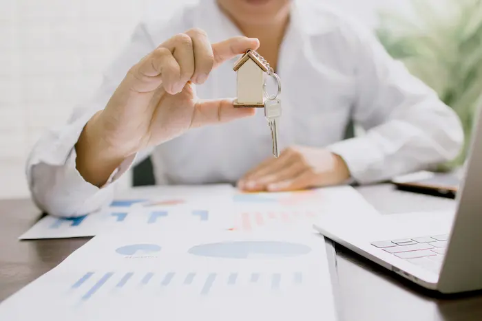 Personne tenant clé en forme de maison devant graphiques financiers, image illustrant l’assurance prêt immobilier.