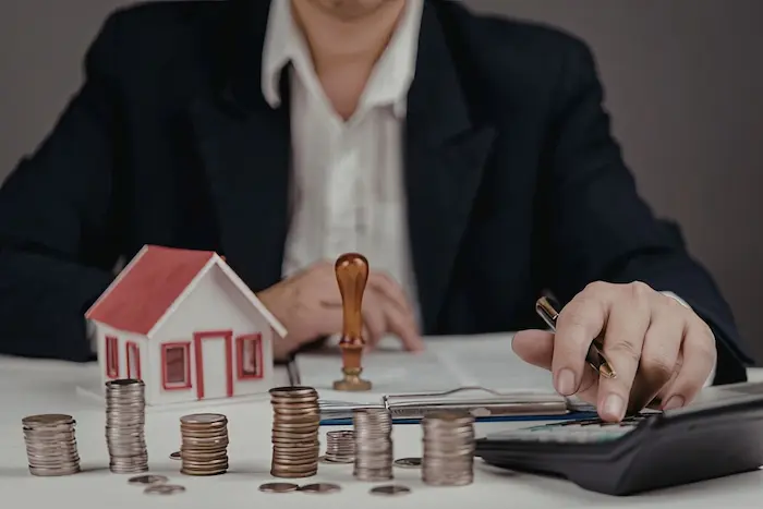 Personne calculant un projet immobilier neuf avec maquette de maison et pièces, illustrant les avantages PTZ pour financer un logement.