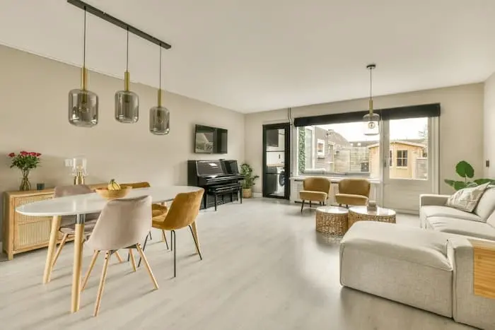 Salon moderne décoré de plusieurs exemples de bien meuble comme un canapé d'angle gris une table à manger ovale et des chaises en velours dans un espace lumineux.