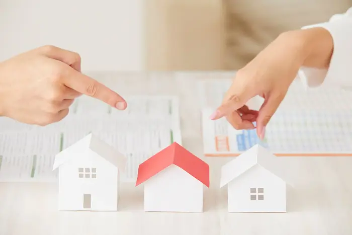Deux mains désignent des maquettes de maisons sur des documents immobiliers illustrant la réflexion faut il acheter en VEFA aujourd’hui.