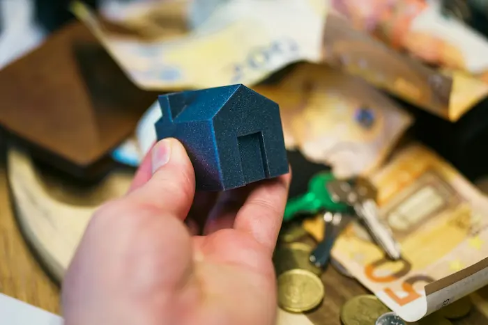 Personne en costume tenant une maquette de maison, image illustrant l’accompagnement d’un courtier pour obtenir un prêt immobilier sans apport.