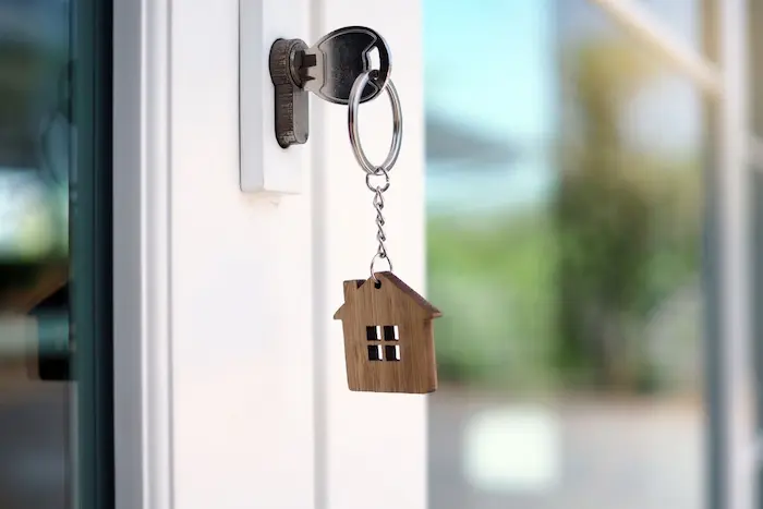 Clé insérée dans une porte avec porte-clés maison en bois illustrant garantie VEFA et sécurité lors d’un achat immobilier neuf.