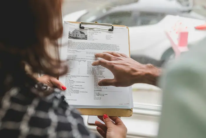 Gros plan sur fiche de maison discutée par deux individus, scène évoquant l’étape du compromis de vente.