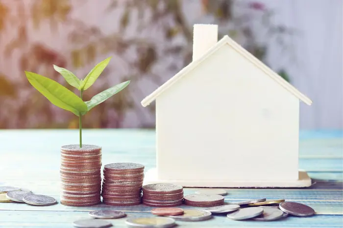 Piles de pièces avec une maison en bois, illustrant la construction d’un plan de financement immobilier pour concrétiser un projet d’achat.