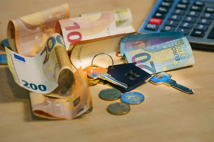 Clés de maison avec porte-clés, billets et pièces en euros sur table illustrant le financement et la gestion d’un prêt immobilier.