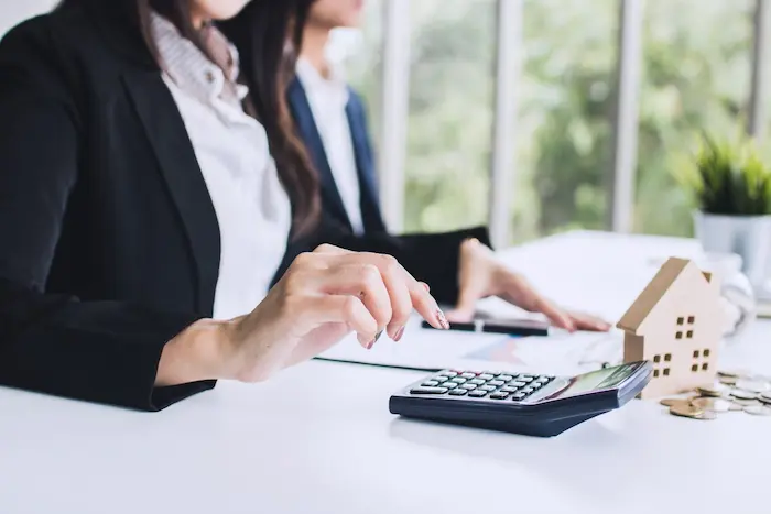 Deux professionnels calculent avec une maquette de maison et des pièces, illustrant le prêt immobilier conçu pour accompagner les primo-accédants.