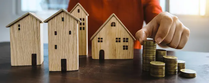Petites maisons en bois posées près de piles de pièces dorées, image évoquant la simulation d’un prêt immobilier avec l’aide du PTZ.