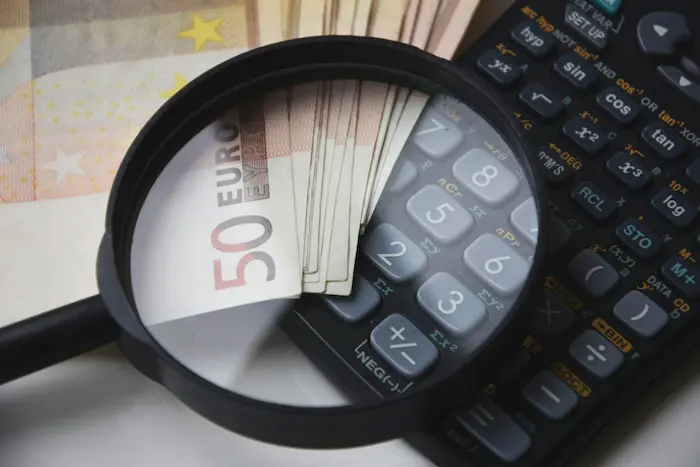 Gros plan sur billets de 50 euros avec loupe et calculatrice, image illustrant le prêt relais immobilier et l’analyse financière pour achat et vente.