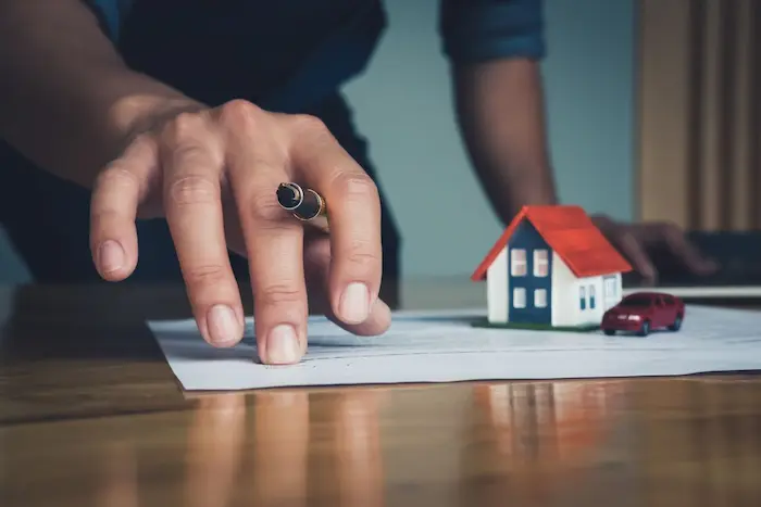 Main pointant un contrat avec maison miniature et voiture rouge, image symbolisant la simulation PTZ pour financer un premier achat immobilier.