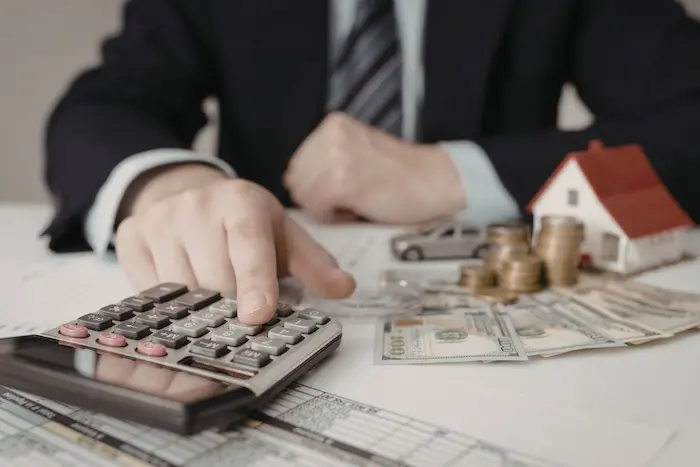 Bureau avec documents financiers, maison miniature, voiture et calculatrice représentant simulateur de mensualités de crédit immobilier et prêt auto.