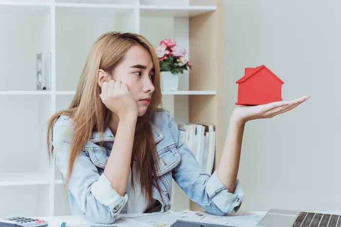 Personne assise avec une maquette de maison rouge, papiers et calculatrice sur le bureau illustrant les litiges VEFA