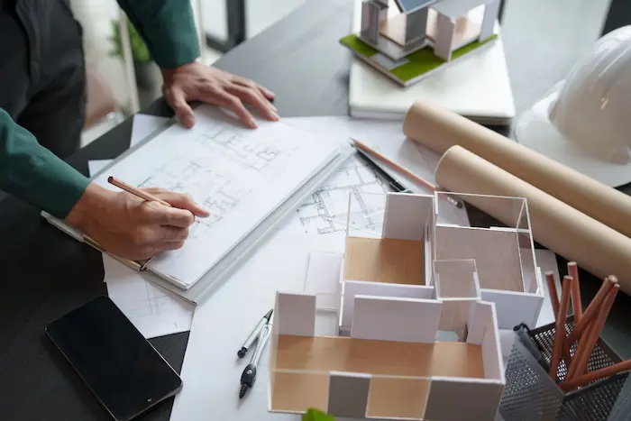 Un architecte travaille sur des plans avec maquette et casque, illustrant le TMA VEFA qui permet de personnaliser un logement neuf avant sa livraison.