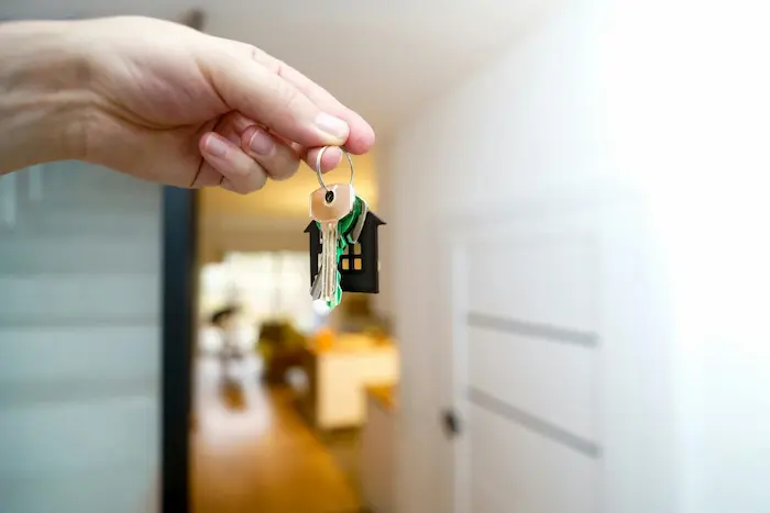 Main tenant un trousseau de clés avec porte-clés maison noire, symbole de remise de clés lors d’un achat d’appartement neuf à Montpellier.