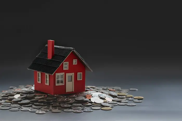Petite maison rouge posée sur des pièces, image illustrant le financement d’une construction neuve avec prêt à taux zéro.