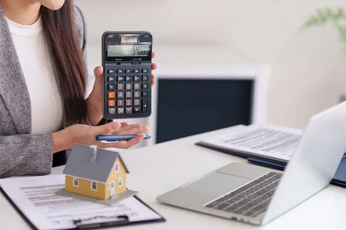 Personne en costume calcule 540000 avec un grand simulateur de mensualités de crédit immobilier sur bureau avec maison miniature et documents financiers.