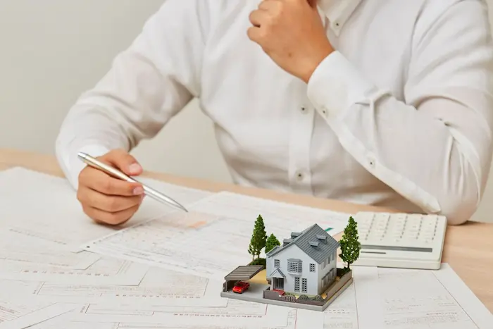 Personne en chemise blanche analyse documents et maison miniature avec calculatrice, image représentant simulation prêt immobilier.